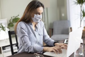 Imagem ilustrativa de mulher mexendo no computador com máscara, para artigo sobre mudanças na hora de comprar imóveis durante a pandemia